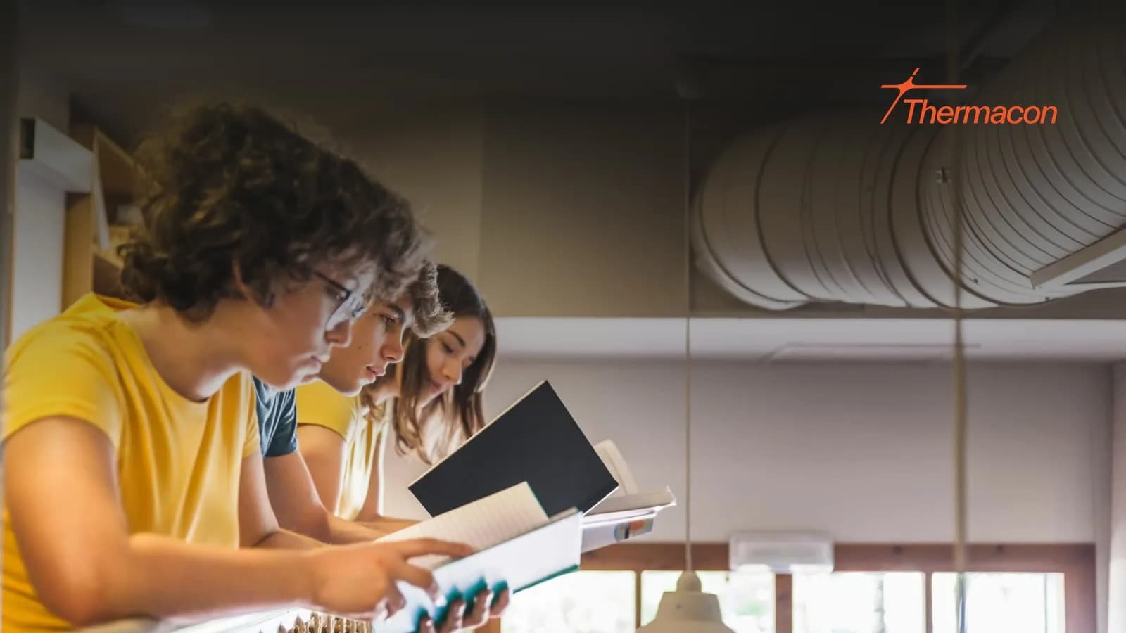 Drie leerlingen lezen samen in een lokaal met ventilatiekanalen onder het plafond